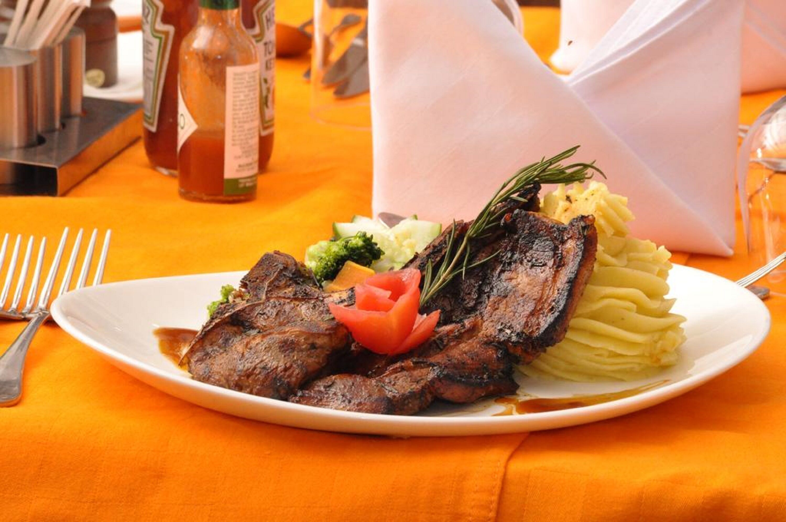 A plate with grilled meat, mashed potatoes, and vegetables on an orange tablecloth.