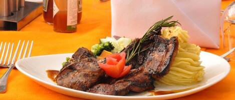 A plate with grilled meat, mashed potatoes, and vegetables on an orange tablecloth.