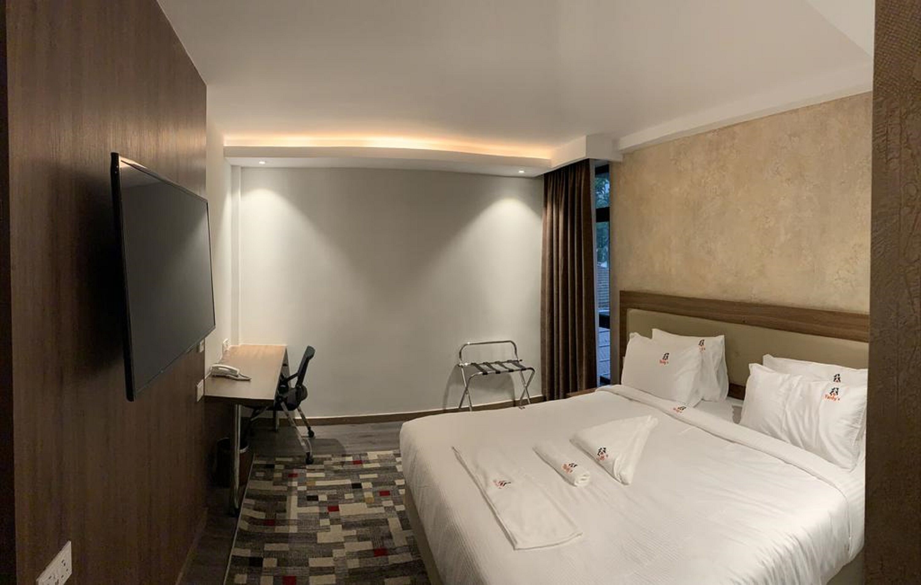 A hotel room with a large bed, a desk, a chair, a TV, and a view of the outdoors.
