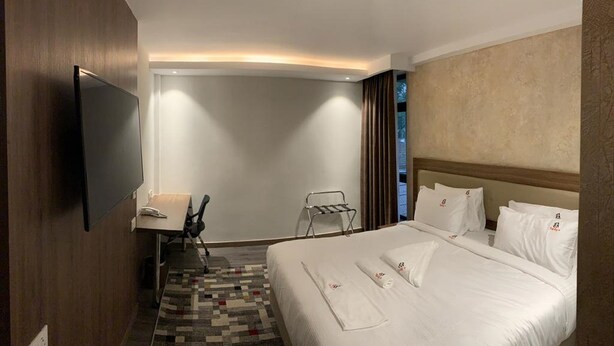 A hotel room with a large bed, a desk, a chair, a TV, and a view of the outdoors. - Taidy's Suites - Nakuru (Nakuru)