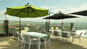 Terraza con mesas al aire libre y sombrillas, con vista a un paisaje urbano.