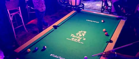 A pool table with a logo and text, surrounded by chairs and tables in a dimly lit room.