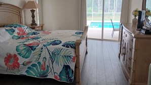 A bedroom with a bed, a dresser, a lamp, and a view of a pool through a sliding glass door. - gulf coast haven !!! (Spring Hill)