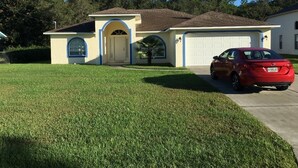 A single-story house with a garage, a red car parked in front, and a well-maintained lawn. - gulf coast haven !!! (Spring Hill)