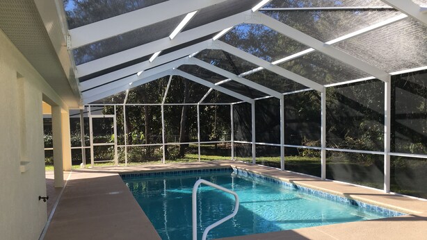 A covered swimming pool with a clear view of the surrounding trees and a concrete deck. - gulf coast haven !!! (Spring Hill)