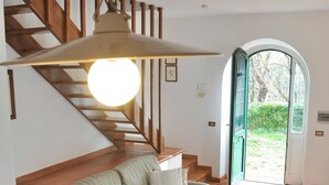 A spacious living area with a sofa, armchair, and a table. A staircase with wooden railings leads to an outdoor area. - Montecasciano Margherita (CAPRANICA)