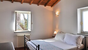 A bedroom with a wooden ceiling, a bed with white linens, a nightstand with a lamp, a window with a view of trees, and a radiator. - Montecasciano Margherita (CAPRANICA)