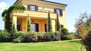 Un bâtiment à deux étages doté d’un balcon, entouré de verdure et d’une pelouse bien entretenue.