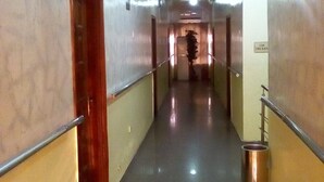 A long, narrow hallway with a shiny floor, metal handrails on both sides, and a door on the left.