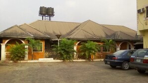 A building with a water tank on the roof, a car parked in front, and palm trees in the yard.