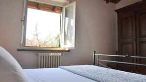 A bedroom with a bed, a window, a radiator, and a wooden wardrobe.