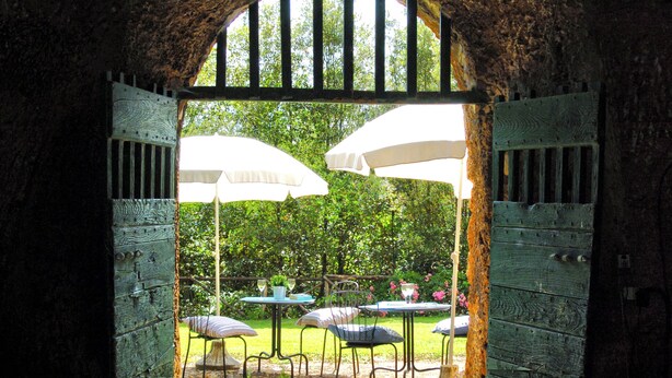 An open archway leading to an outdoor seating area with tables and chairs, surrounded by greenery.