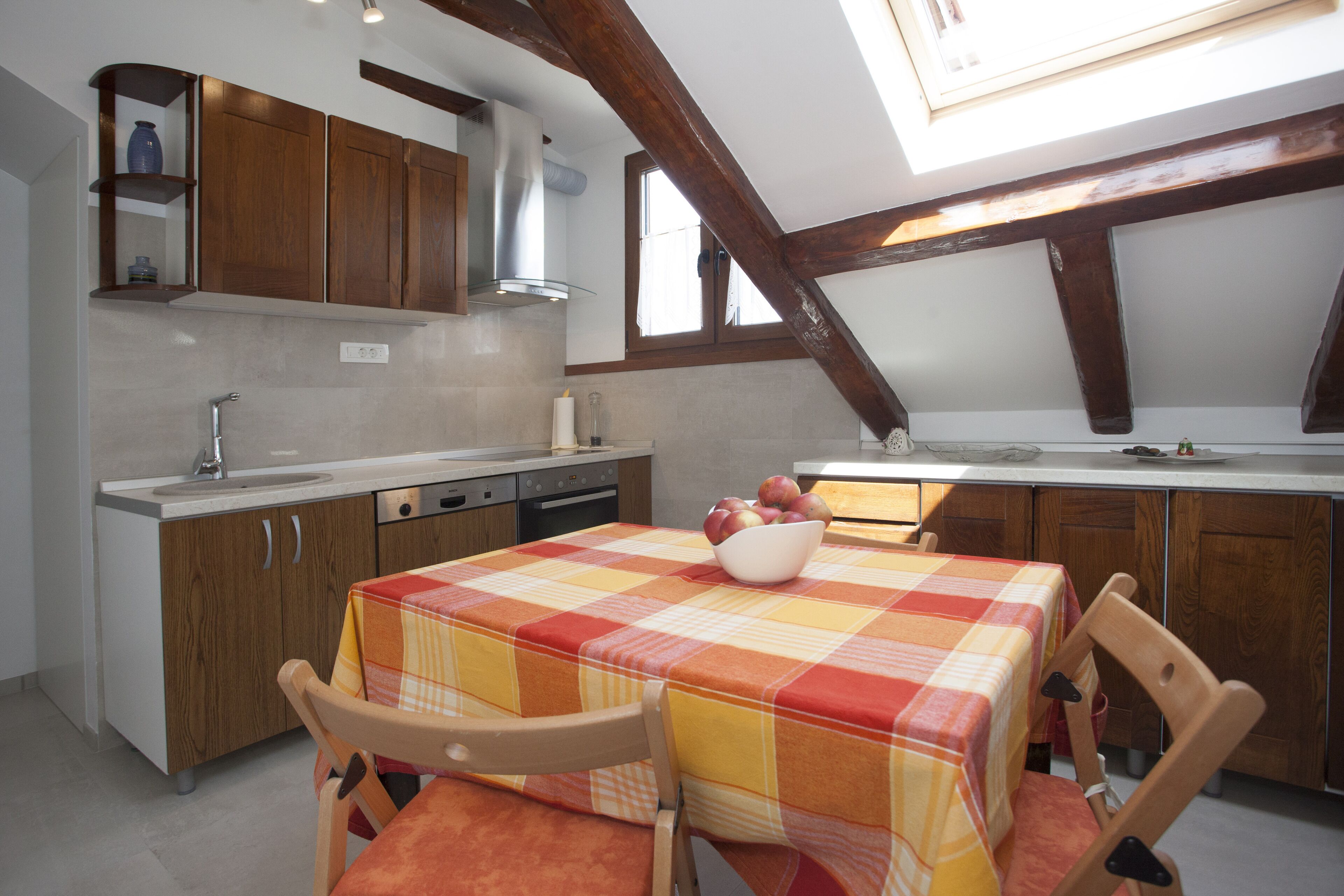 A kitchen with wooden cabinets, a checkered tablecloth, and a bowl of fruit on the table.