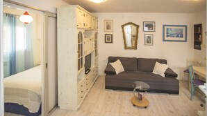 En stue med sofa, TV, skab og spiseplads.