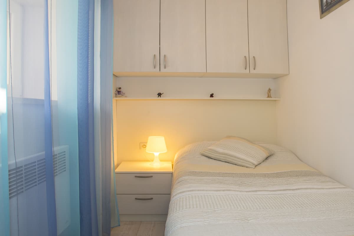 Une chambre à coucher avec un lit, une table de chevet avec une lampe, une armoire et une fenêtre avec des rideaux.