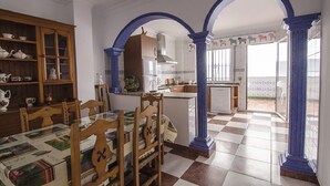 Un coin repas avec une table en verre et des chaises en bois, une cuisine avec des colonnes bleues et un sol à carreaux.