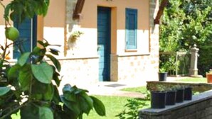 A single-story building with a stone facade, a blue door, and a small porch area. - Montecasciano Oleandro (Capranica)