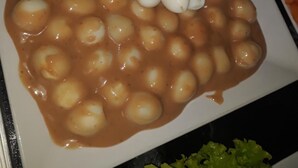 A plate of boiled eggs in a sauce, garnished with a bacon-wrapped apple and grapes.