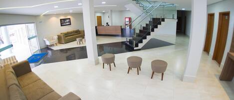 A spacious lobby with a modern staircase, a reception desk, and a seating area with ottomans.