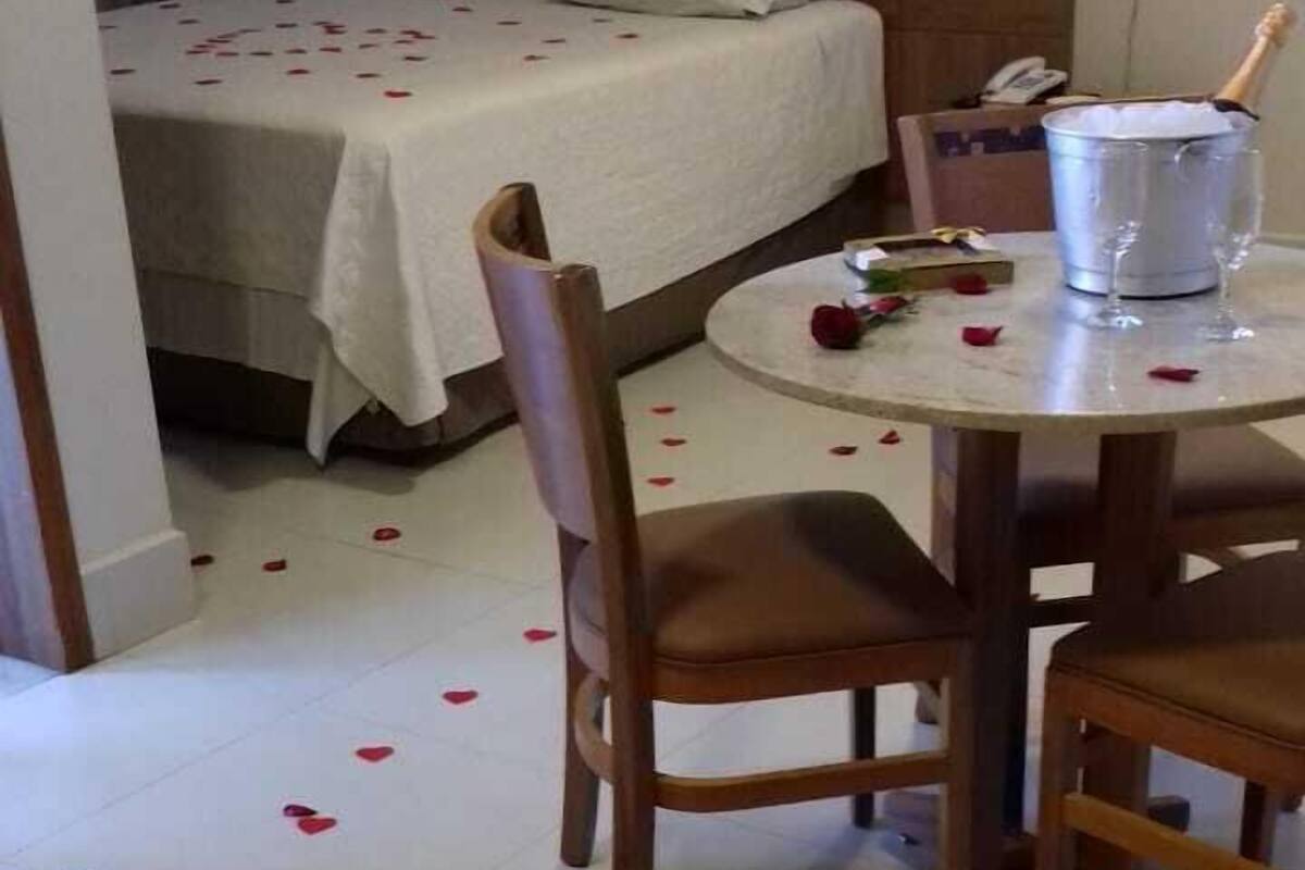 A hotel room with a bed, a dining table with chairs, and a bucket with a bottle.