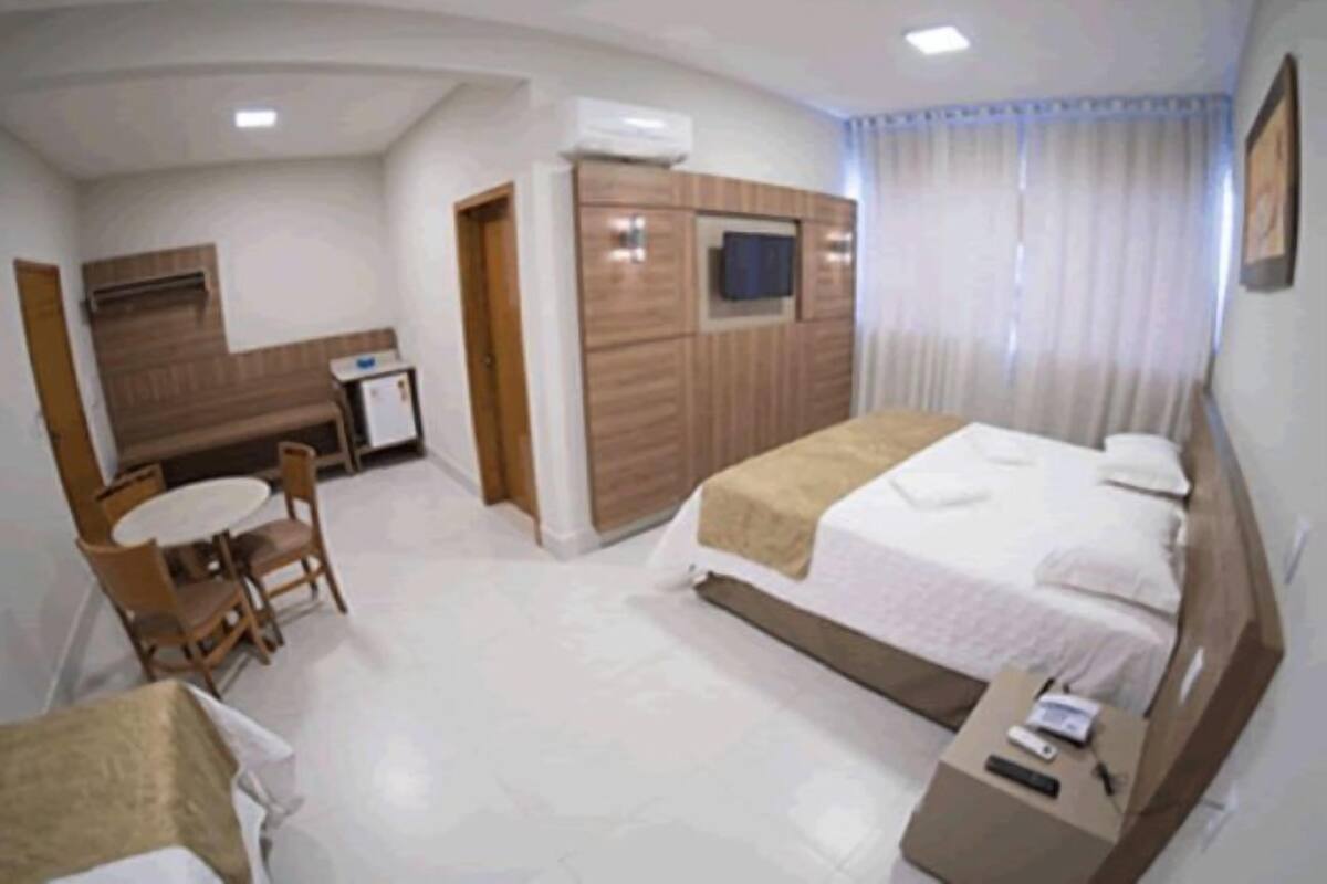 A hotel room with a bed, a desk, a chair, a small table, and a TV mounted on the wall.