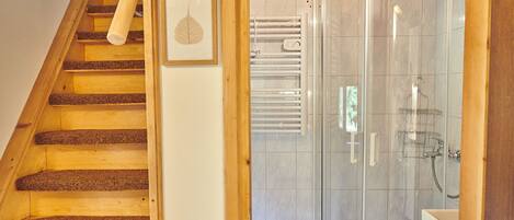 A wooden staircase leading to a bathroom with a glass shower enclosure and a towel rack.