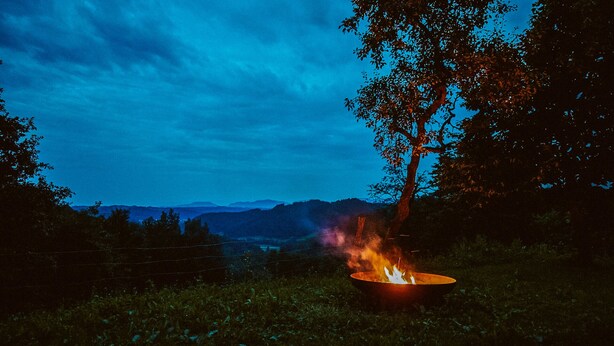 A campfire on a wooden deck with a view of mountains in the background.