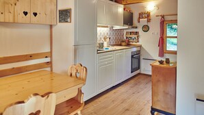 A kitchen with wooden cabinets, a wooden dining table, and a window with a view of greenery.