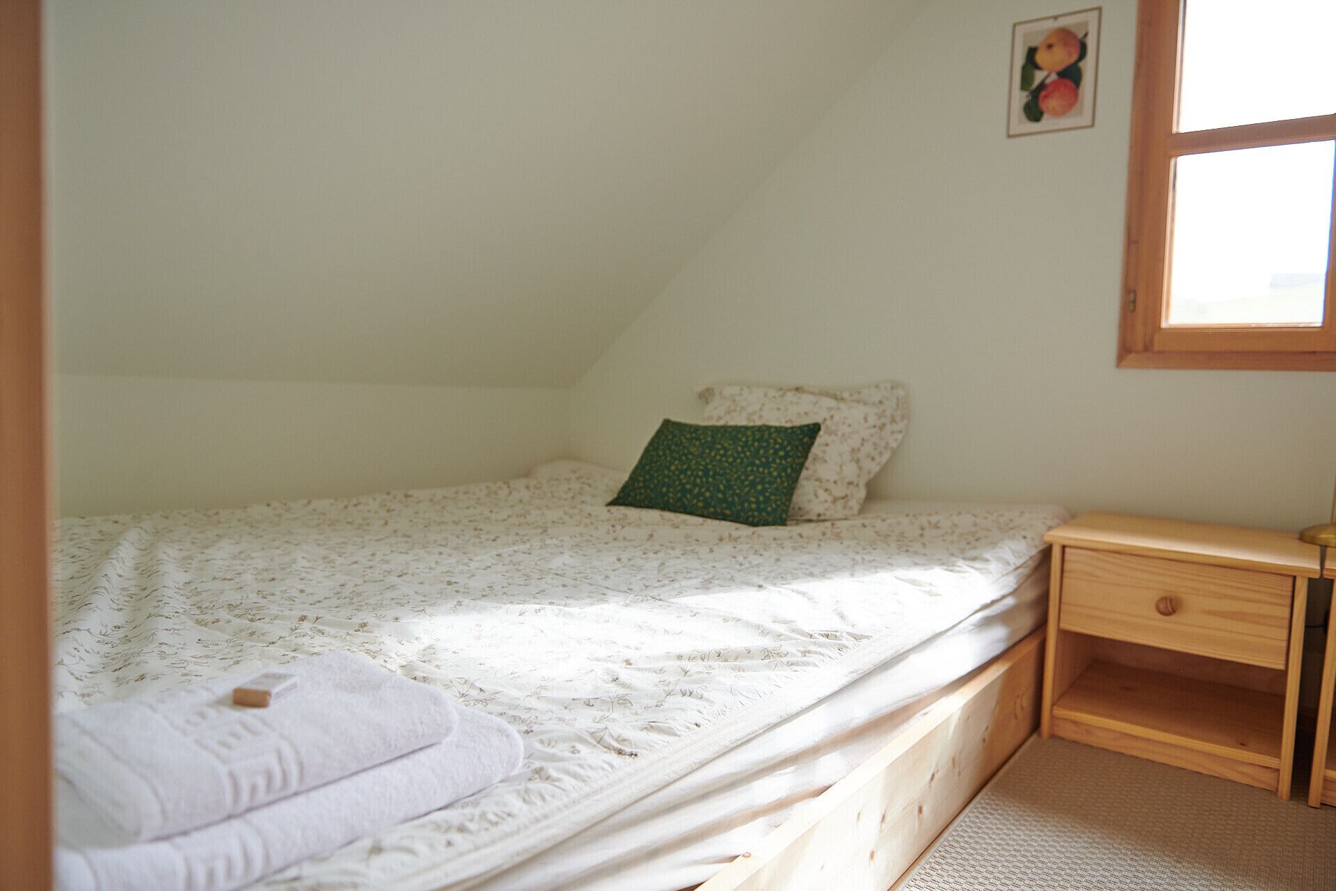 A small, single-bed room with a wooden nightstand and a window.
