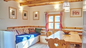 A cozy room with a wooden bench and a dining table, framed pictures on the walls, and a window with curtains.