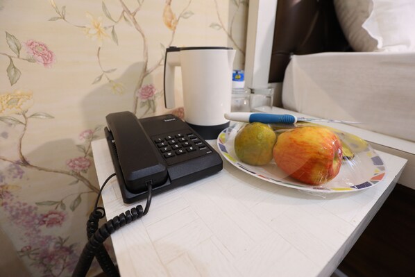 Une chambre d’hôtel avec un téléphone, une assiette de fruits et une machine à café sur la table.