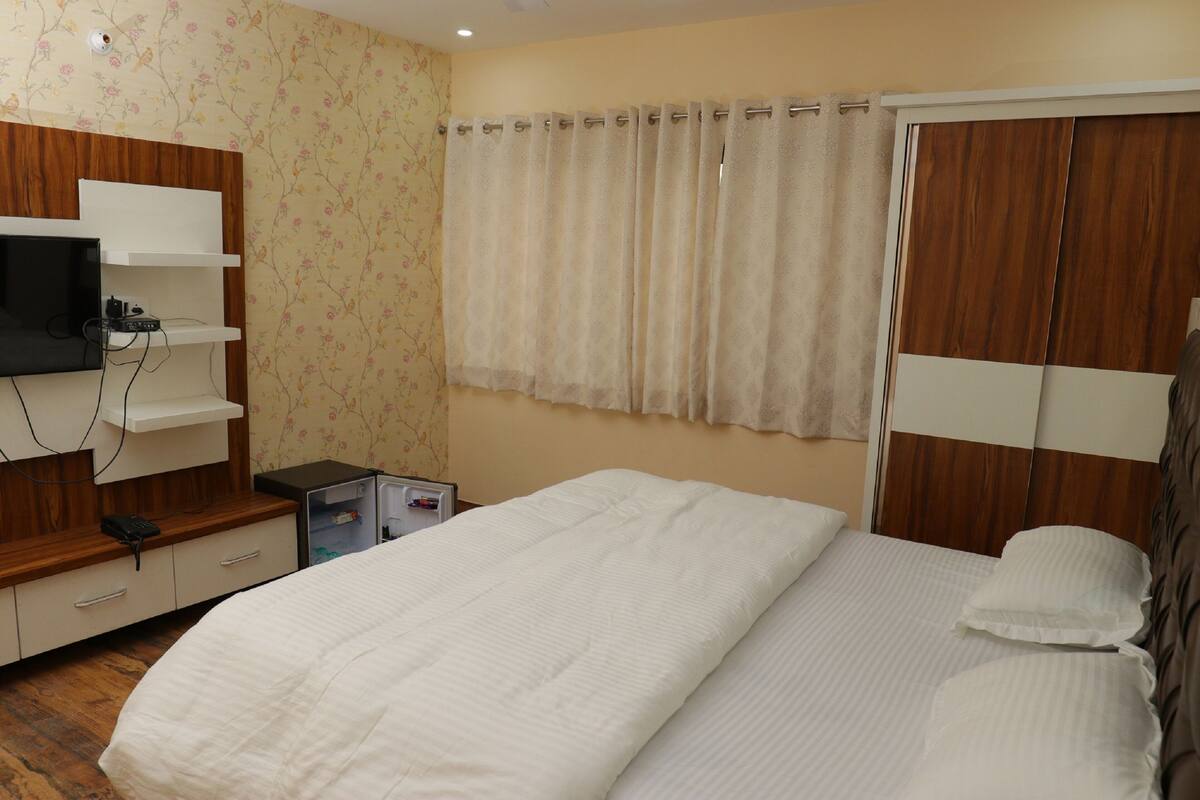 A bedroom with a bed, a TV mounted on a wooden cabinet, a wardrobe, and a curtain.