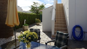 A patio with a table, chairs, a yellow umbrella, and a blue hose.