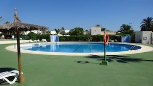 A swimming pool with a lifebuoy, lounge chairs, and a thatched umbrella.