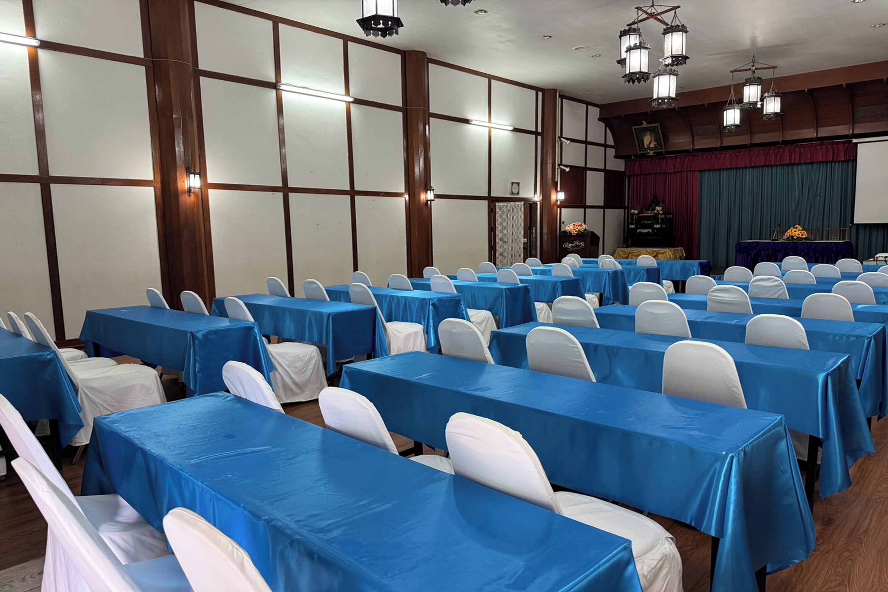 Un salón de conferencias con filas de mesas cubiertas con manteles azules y sillas blancas.