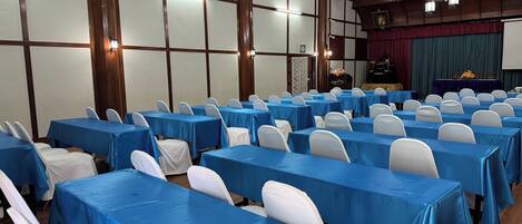 Un salón de conferencias con filas de mesas cubiertas con manteles azules y sillas blancas.