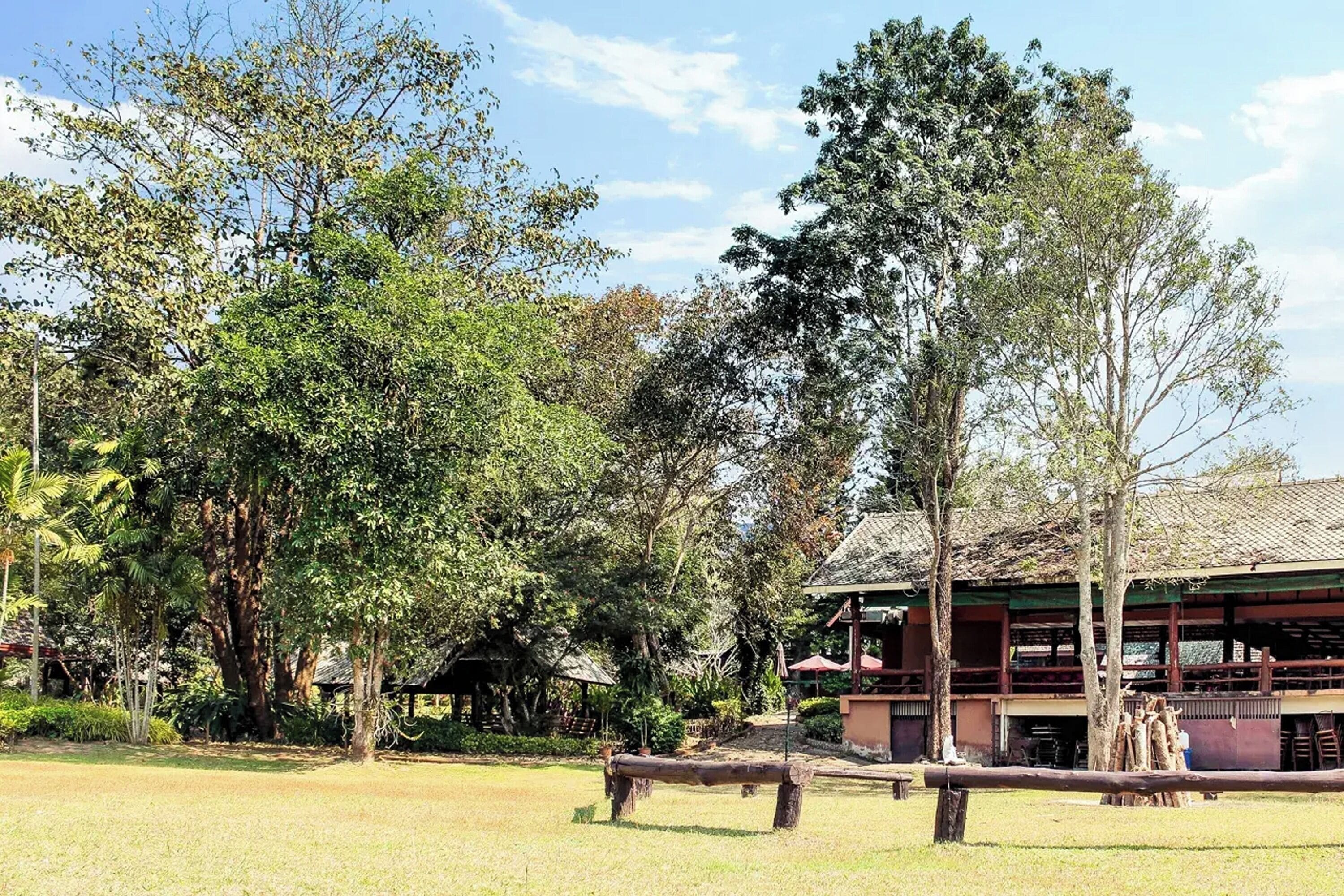 A traditional wooden building with a tiled roof, surrounded by lush greenery and trees.