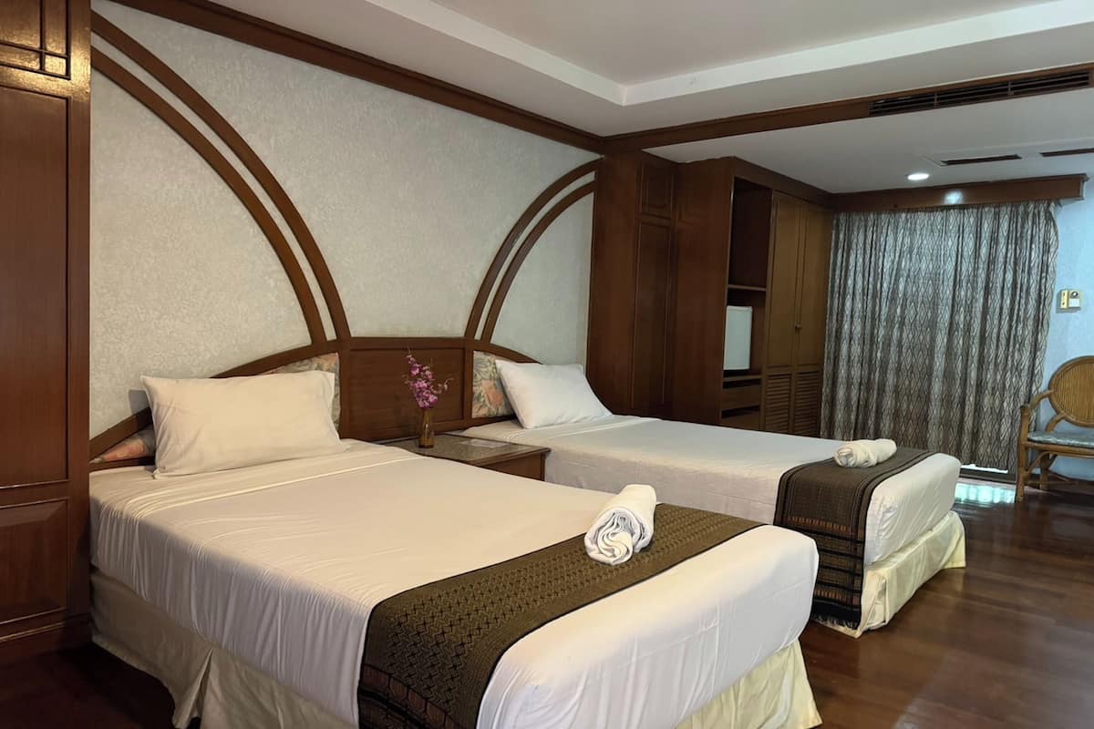 Une chambre d’hôtel avec deux lits, des têtes de lit en bois, une table de chevet, un vase avec des fleurs et une chaise.