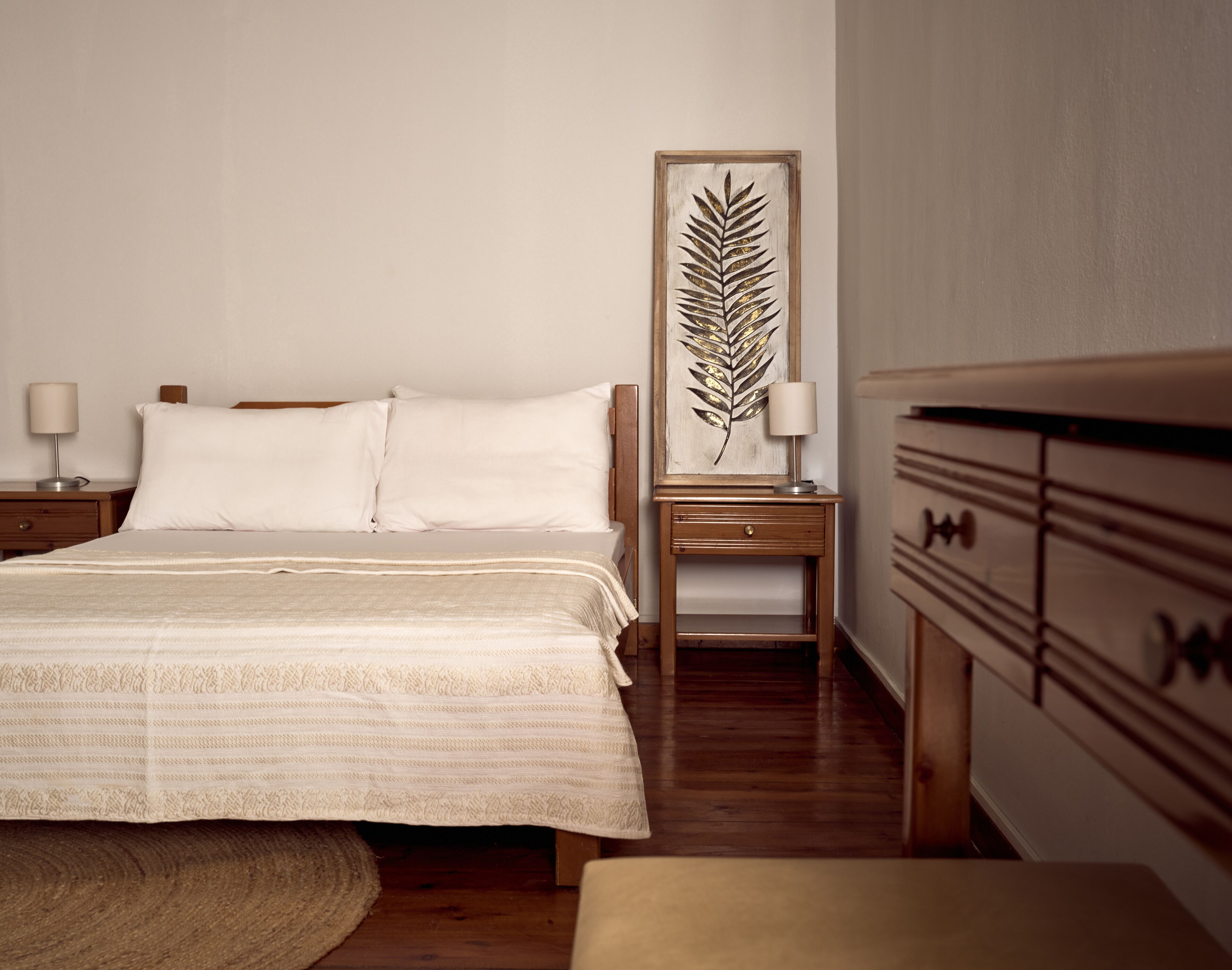 Una camera da letto ordinata con un letto, comodini, una cassettiera e un’opera d’arte con foglie incorniciate.