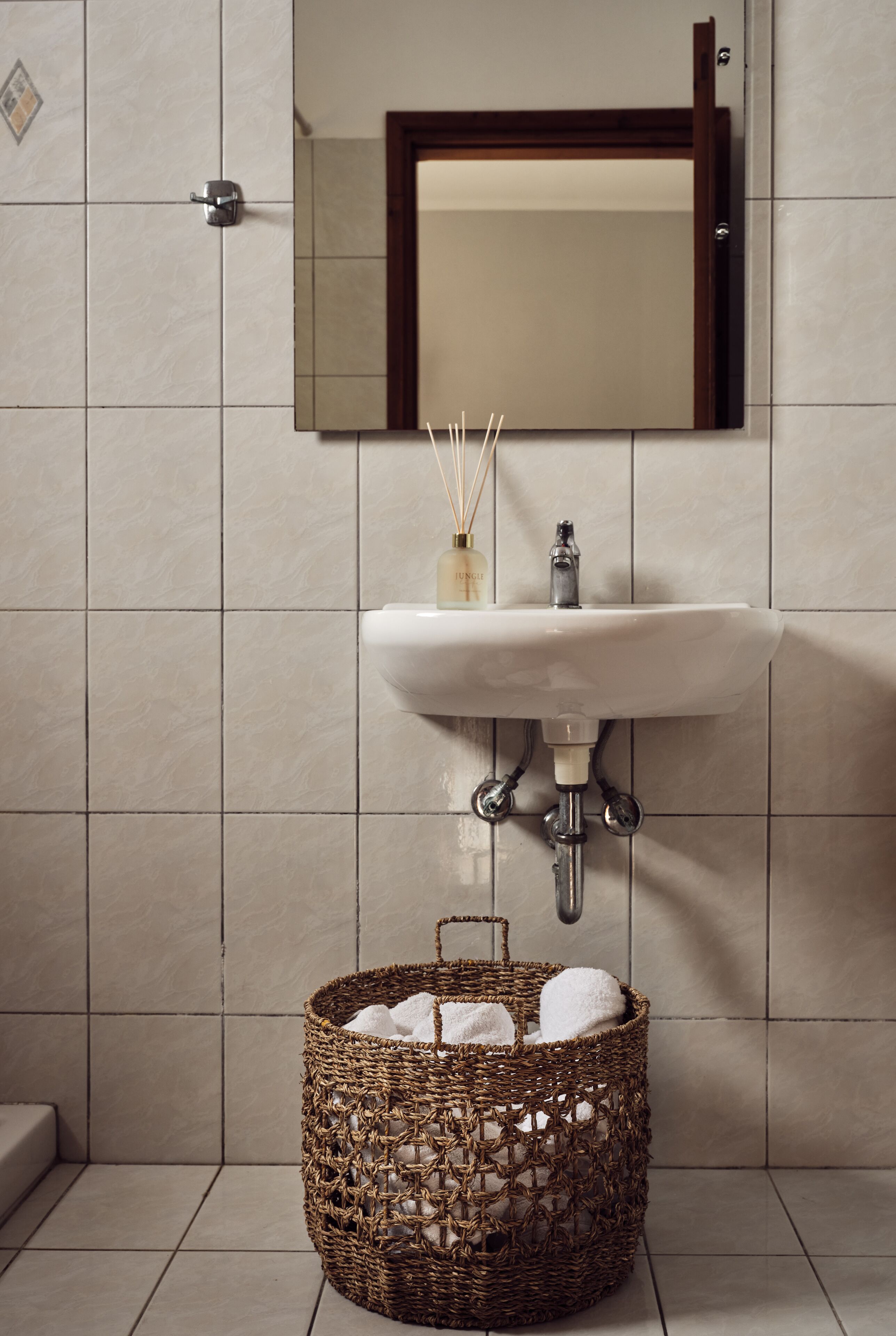 A bathroom with a white sink, a mirror, and a wicker basket with towels.