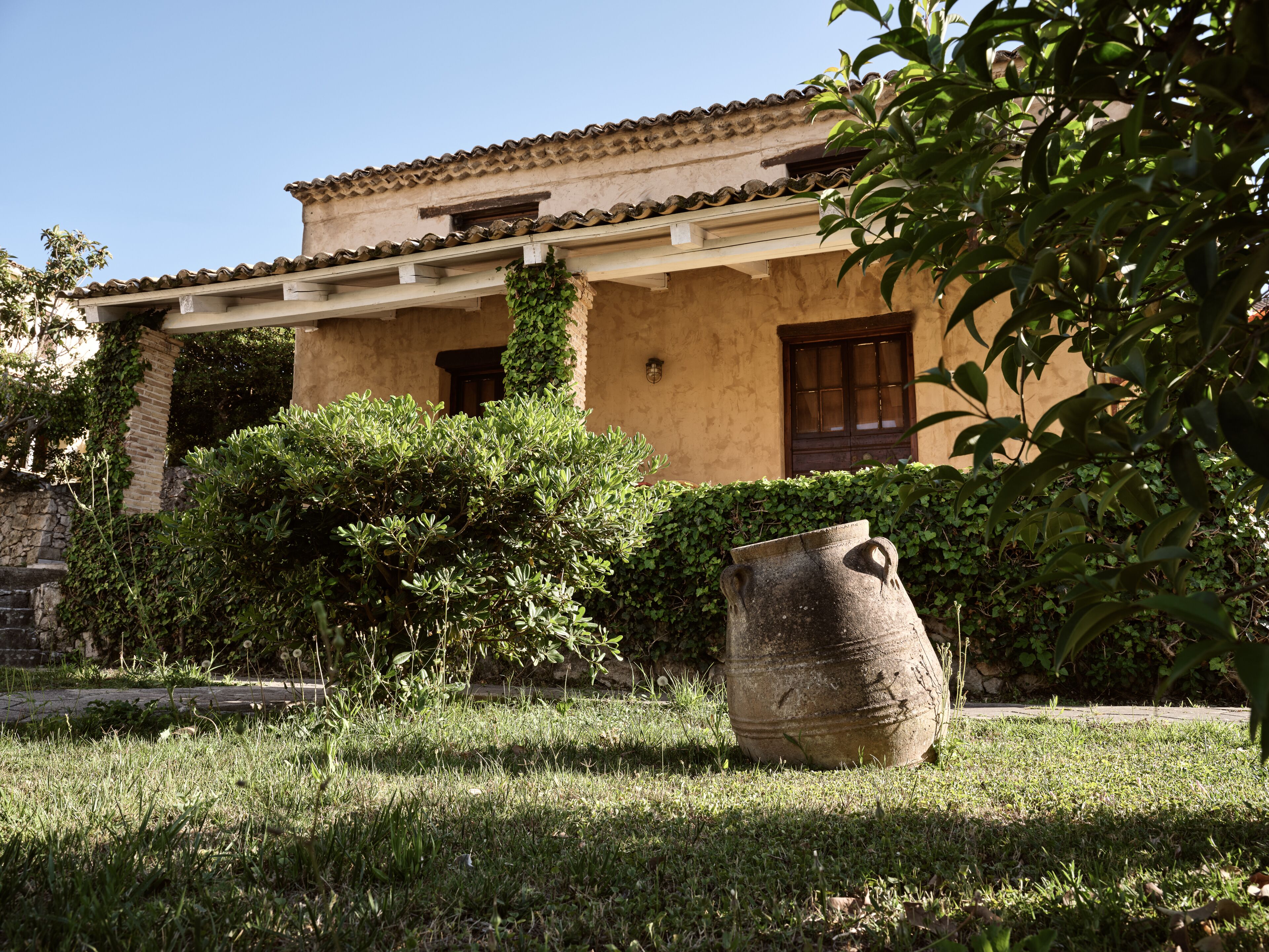 A traditional building with a tiled roof, a stone wall, and a large stone pot in the foreground.