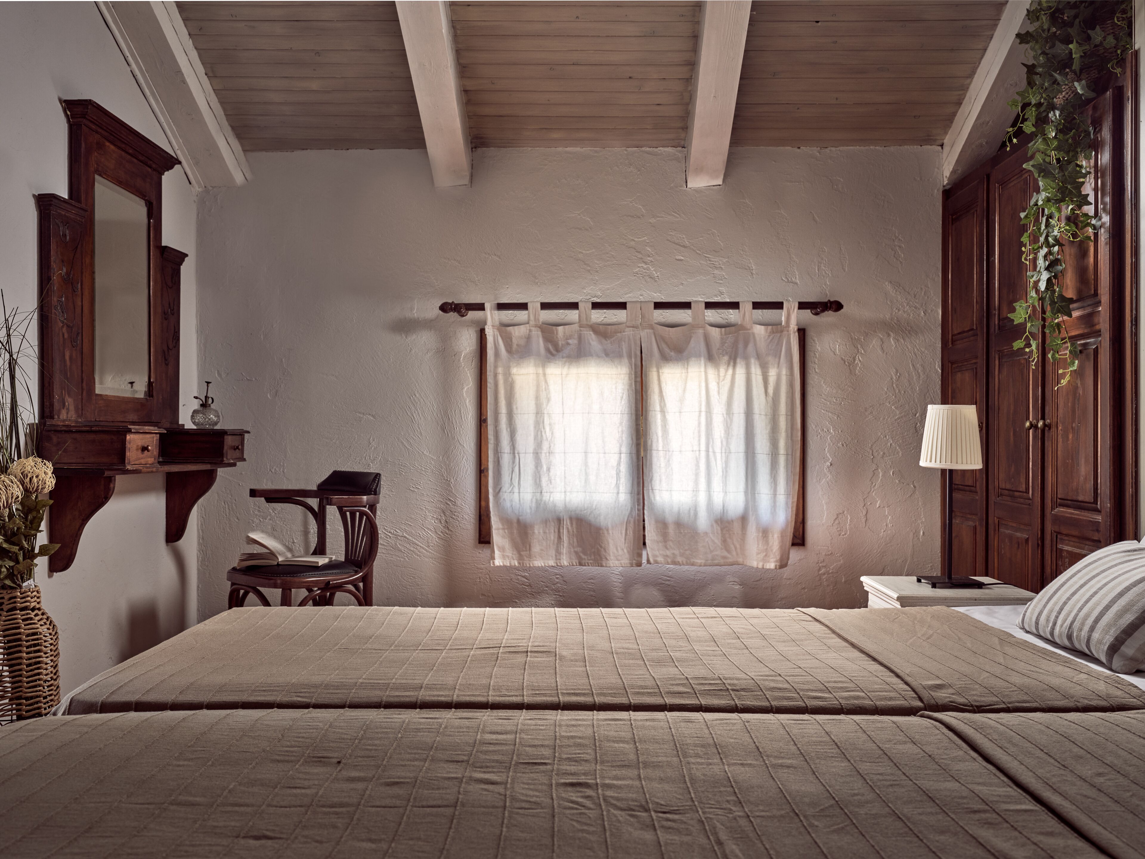 A bedroom with a large bed, a wooden dresser, a chair, a bedside table, and a lamp.