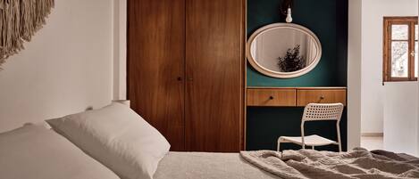 A bedroom with a bed, a wooden wardrobe, a chair, a round mirror, and a green accent wall.