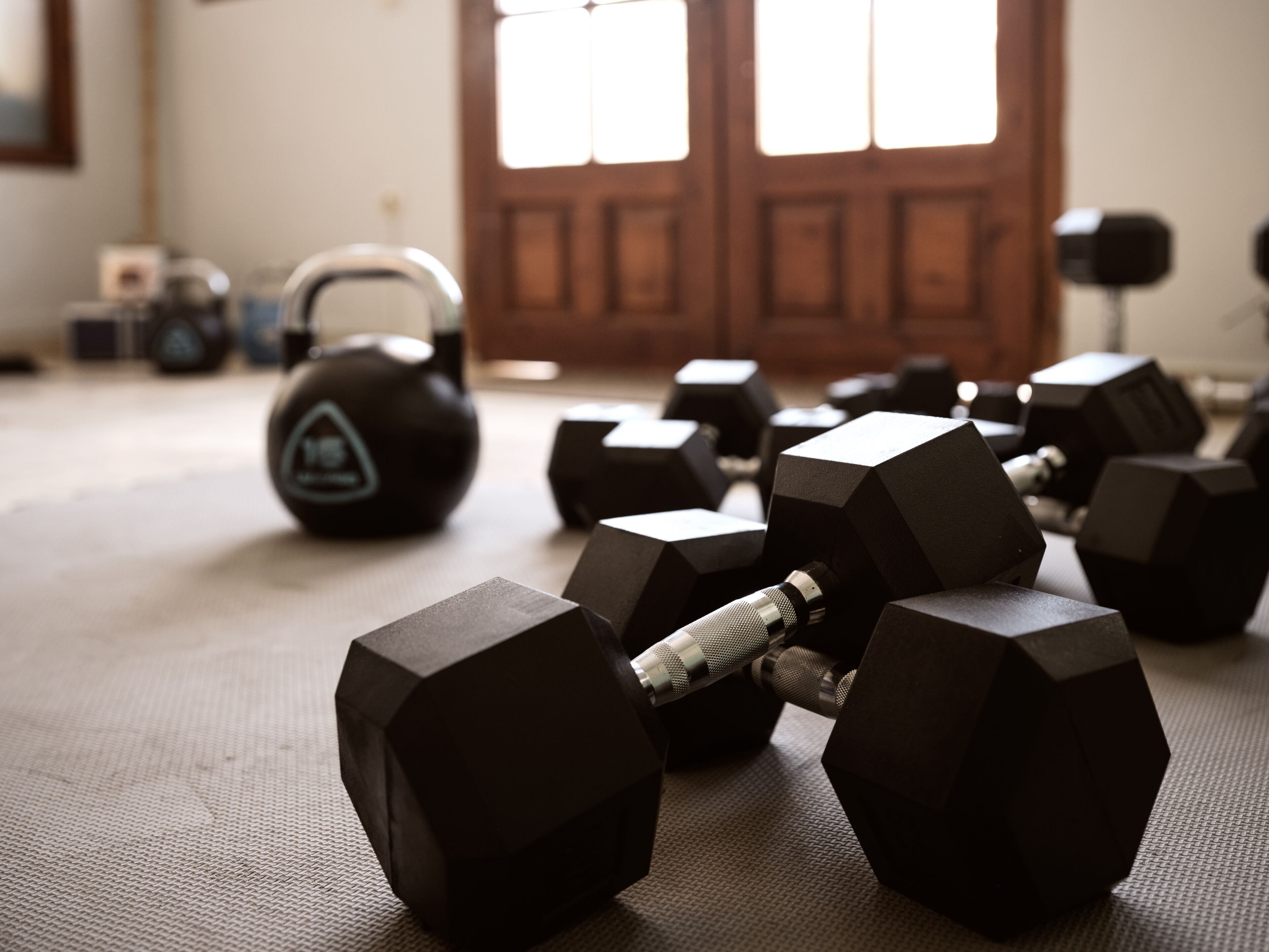 A room with exercise equipment, including dumbbells and a kettlebell, on a textured floor.