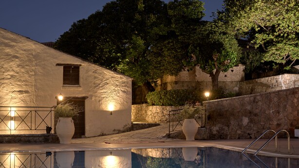 A pool with a stone wall and a building with a door and windows.