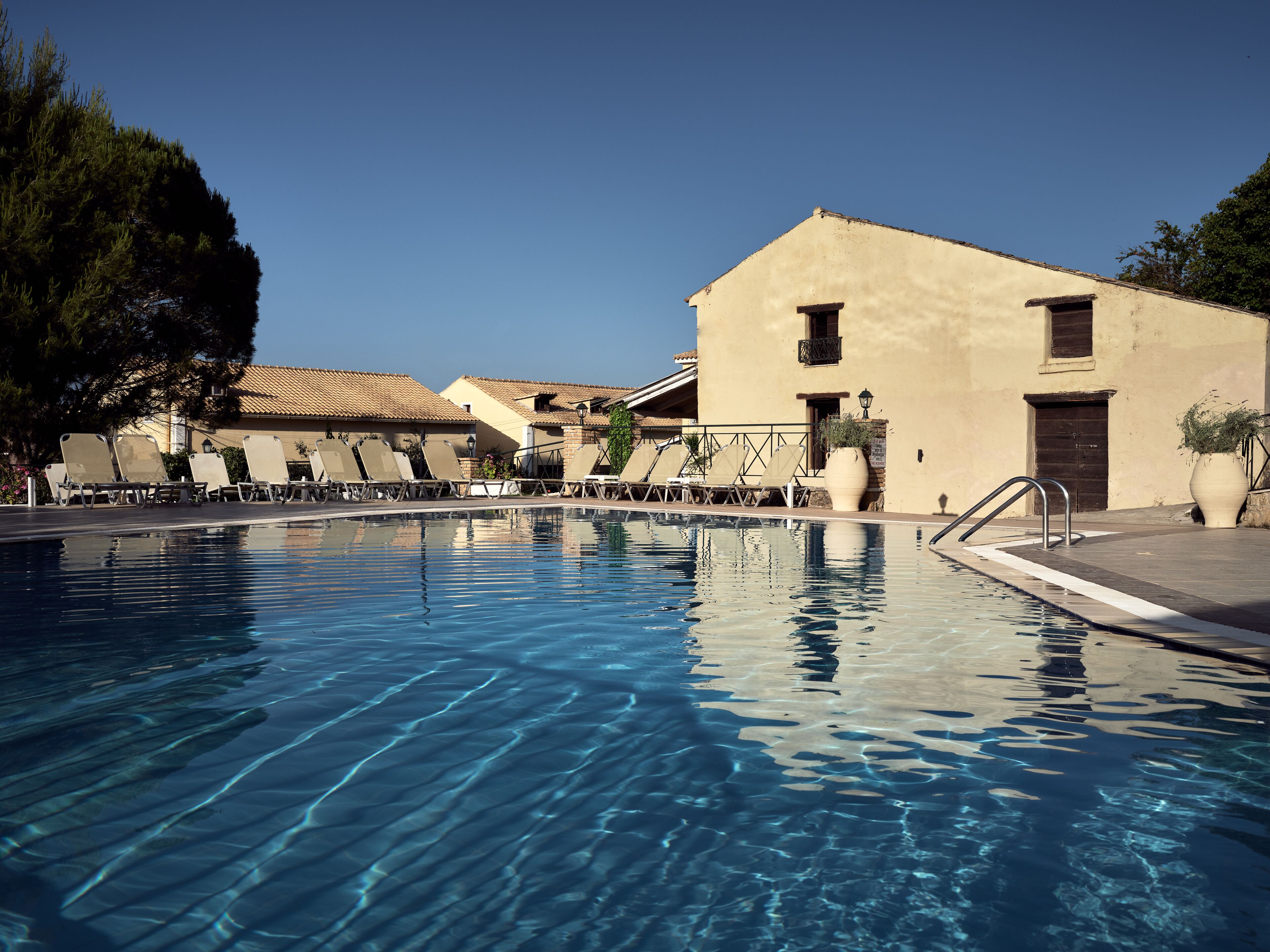 A swimming pool with lounge chairs and a building with a tiled roof.