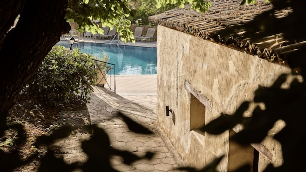 Un chemin de pierre mène à un espace piscine agrémenté d’un mur rustique et offrant une vue sur la piscine.