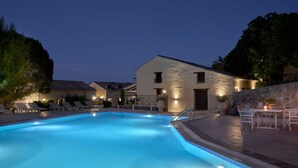 A swimming pool with lounge chairs and a stone building with a tiled roof.