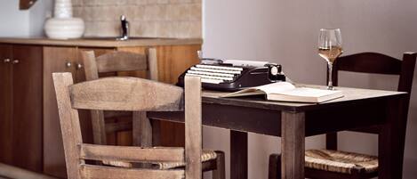 A dining area with wooden chairs and a table, a typewriter, and a wine glass.