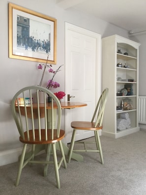 A room with two green chairs, a small round table, a white door, and a bookshelf with various items. - Fabulous Apt Historic House St Aubin (St. Brelade)